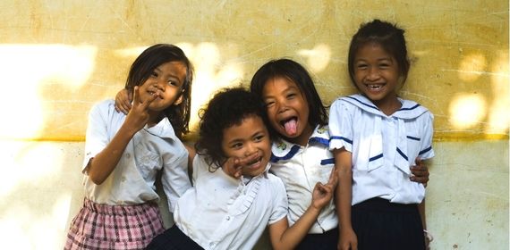 Four school girls standing against a yellow wall smiling cheekily - GapGuru