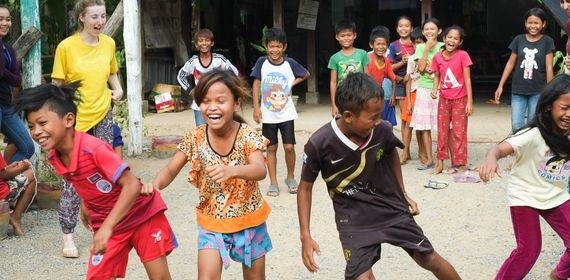 A group of Cambodian children racing in the street laughing with lots of others cheering on - GapGuru