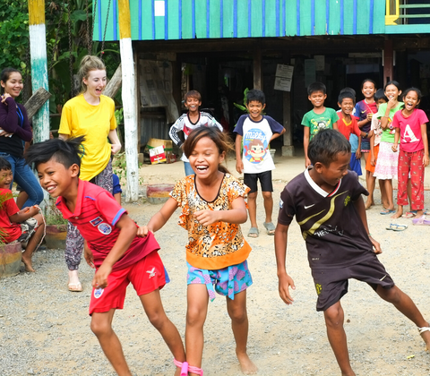 A group of Cambodian children racing in the street laughing with lots of others cheering on - GapGuru