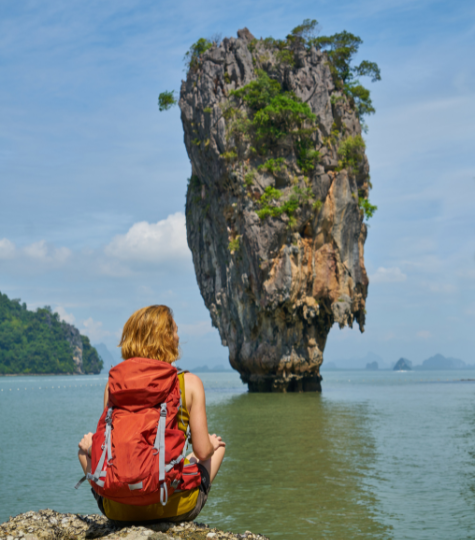 An impressive rock feature off the Thai coast with a backpacker sitting admiring it - GapGuru