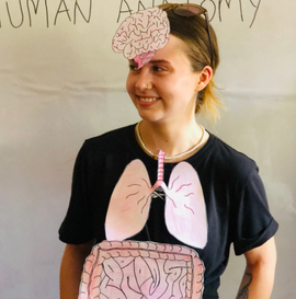 A GapGuru gap year student standing at the front of a class with different parts of the human anatomy stuck to her body - GapGuru